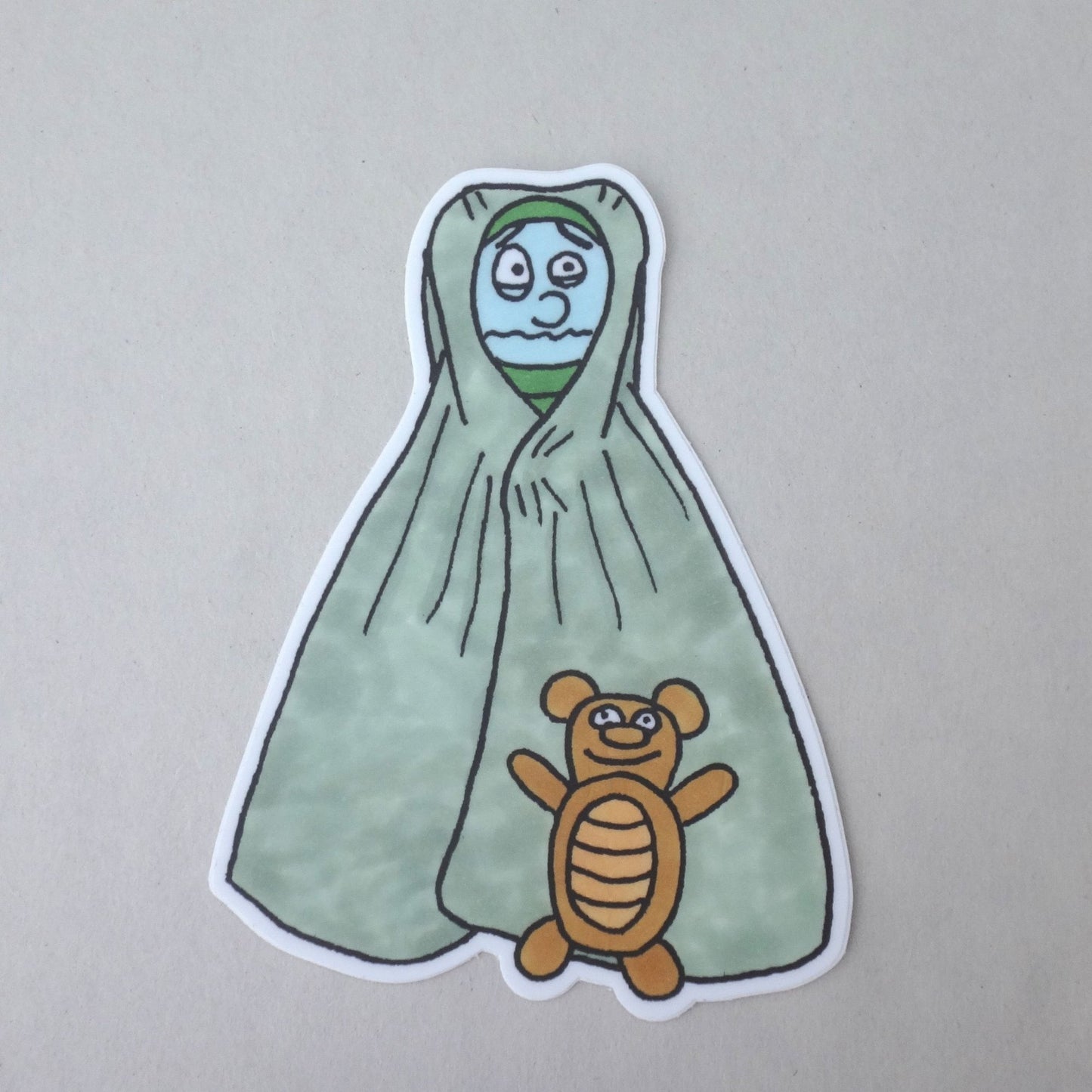 A sticker of Bug Boy Wrapped in a blacket with his teddy bear